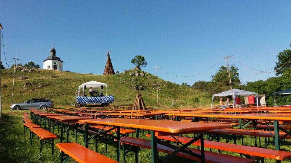 Festgelände mit Bierbänken und aufgeschichtetem Johannifeuer vor der Kapelle am Hügel
